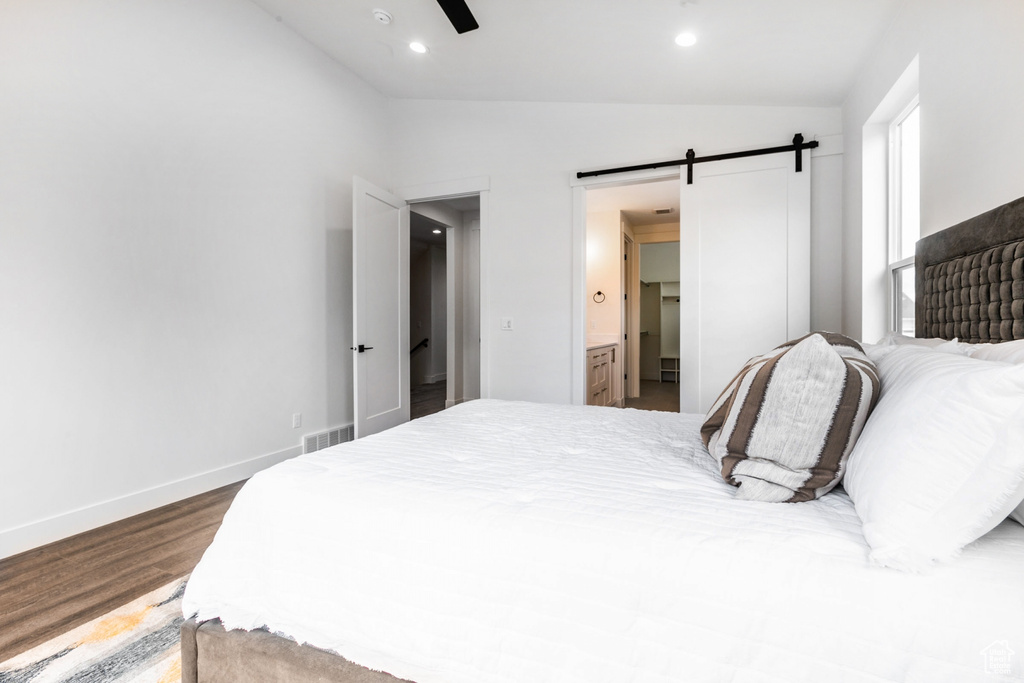 Bedroom featuring ceiling fan, a barn door, ensuite bathroom, lofted ceiling, and wood-type flooring
