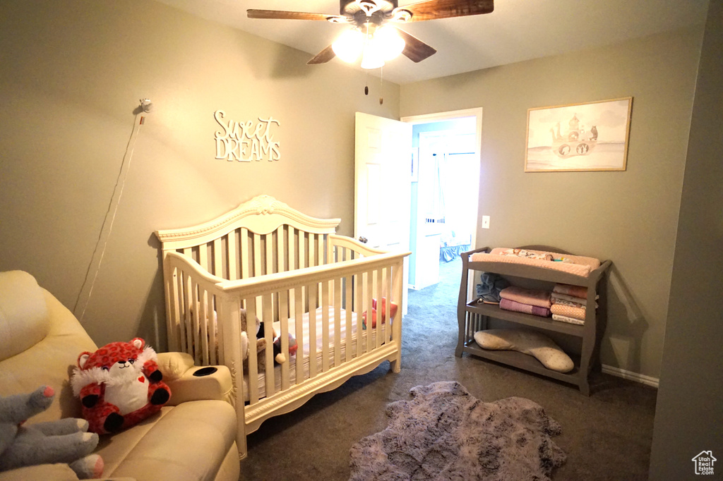 Bedroom featuring dark colored carpet, a nursery area, and ceiling fan