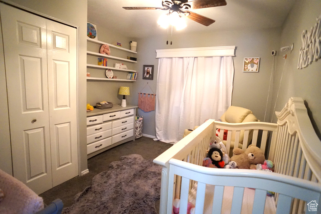 Carpeted bedroom featuring a closet, ceiling fan, and a crib
