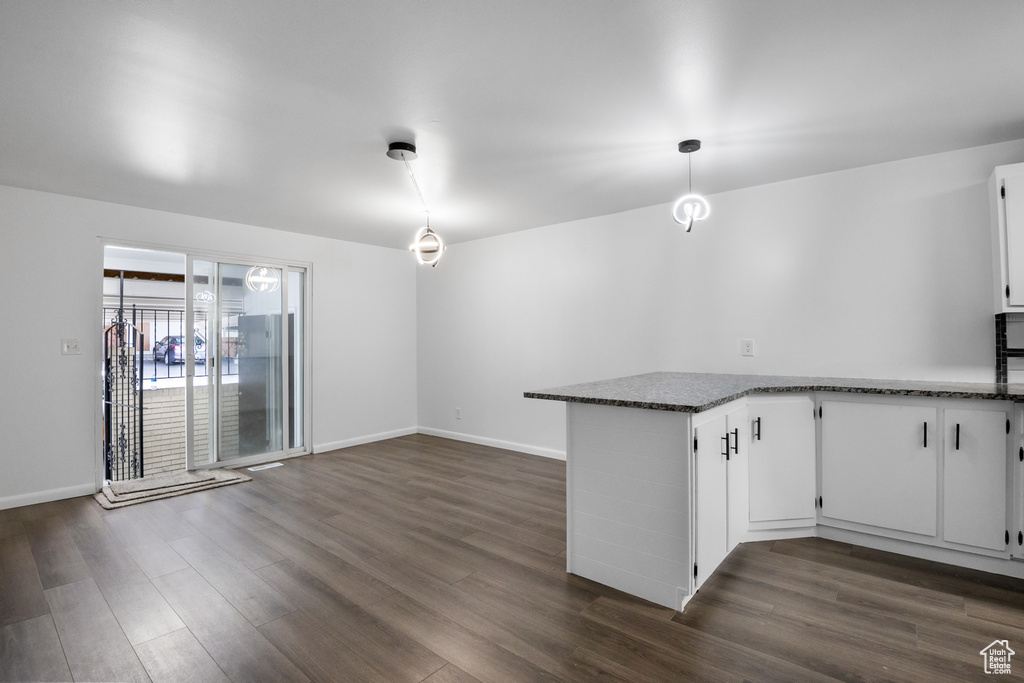 Kitchen with kitchen peninsula, dark hardwood / wood-style floors, dark stone countertops, white cabinets, and pendant lighting