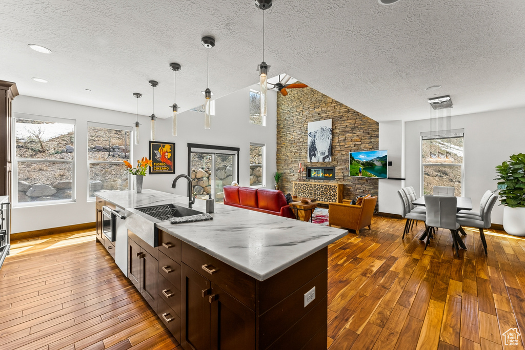 Kitchen with pendant lighting, a kitchen island with sink, light stone countertops, hardwood / wood-style floors, and a stone fireplace