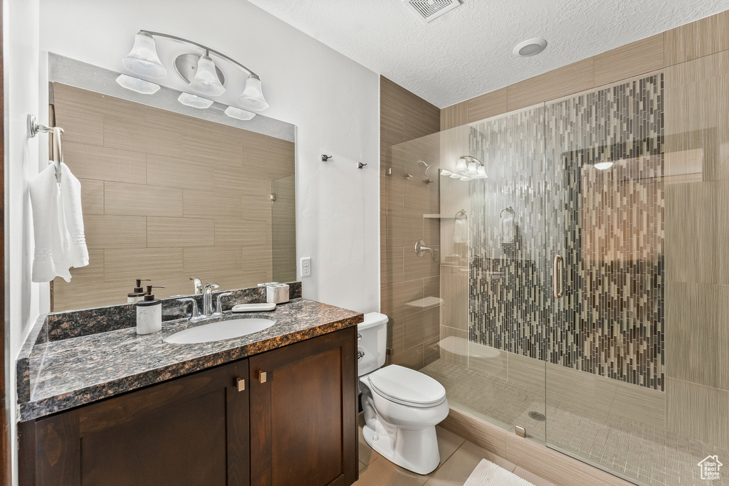 Bathroom with an enclosed shower, oversized vanity, tile flooring, toilet, and a textured ceiling