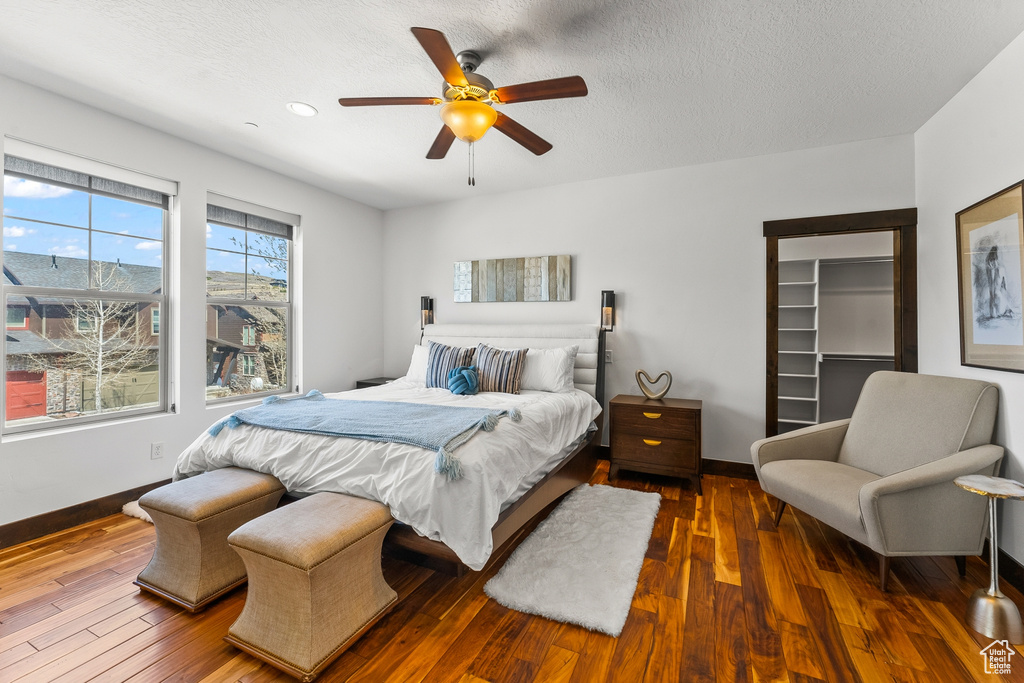 Bedroom featuring a walk in closet, ceiling fan, dark hardwood / wood-style floors, and a textured ceiling