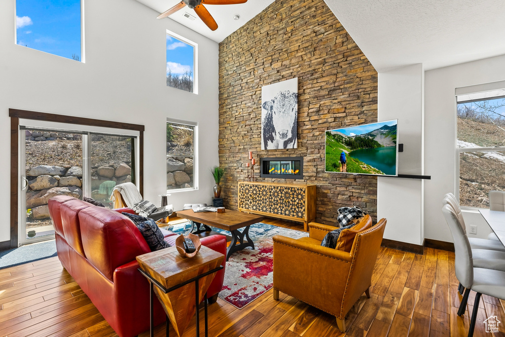 Living room featuring hardwood / wood-style flooring, a stone fireplace, a towering ceiling, and ceiling fan