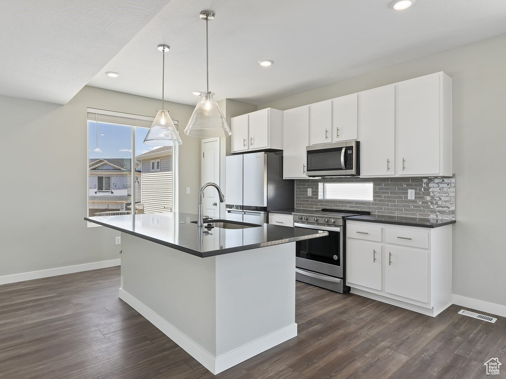 Kitchen featuring a kitchen island with sink, white cabinets, dark hardwood / wood-style flooring, stainless steel appliances, and sink