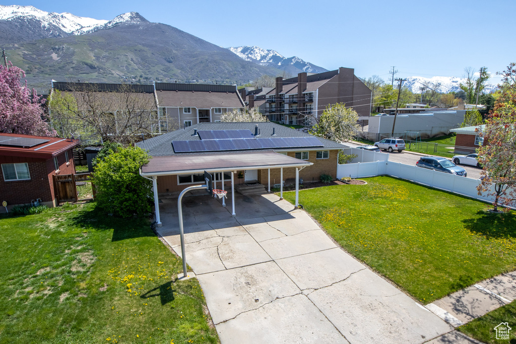 View of front of property with solar panels, a carport, a mountain view, and a front lawn
