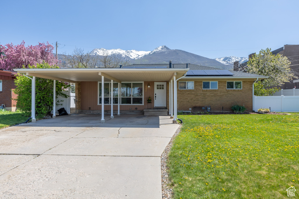 View of front of home featuring a front lawn, a carport, a mountain view, and solar panels