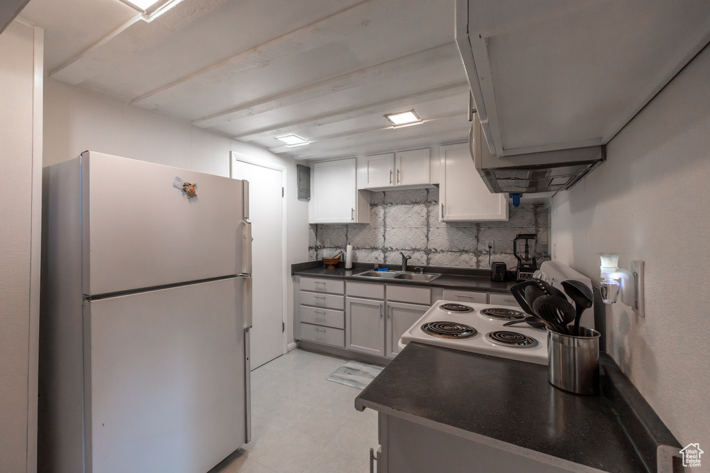 Kitchen featuring white cabinets, white refrigerator, backsplash, sink, and light tile floors