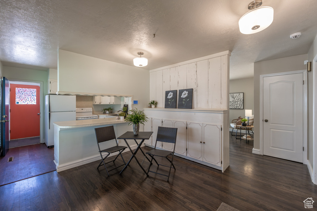 Kitchen featuring a kitchen breakfast bar, white appliances, dark hardwood / wood-style flooring, white cabinetry, and kitchen peninsula