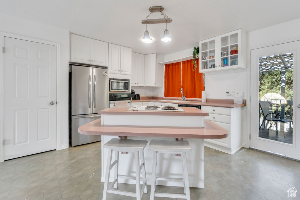 Kitchen with a center island, light tile floors, white cabinetry, decorative light fixtures, and stainless steel appliances