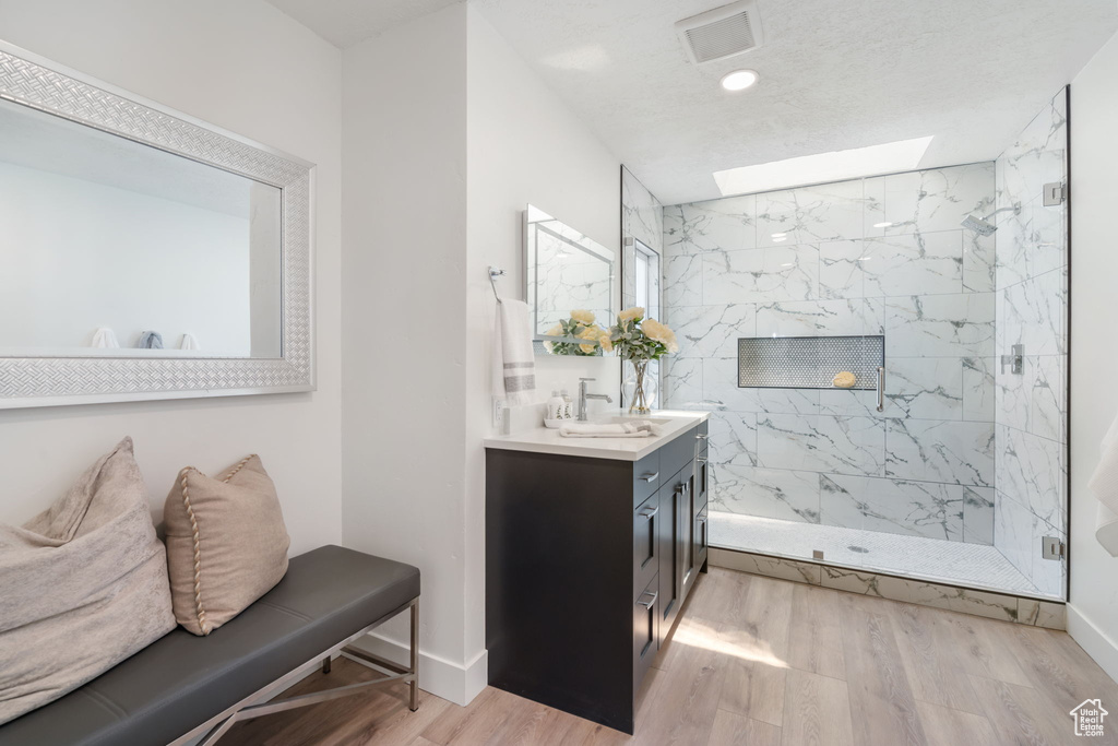 Bathroom featuring a skylight, vanity, hardwood / wood-style flooring, and a tile shower