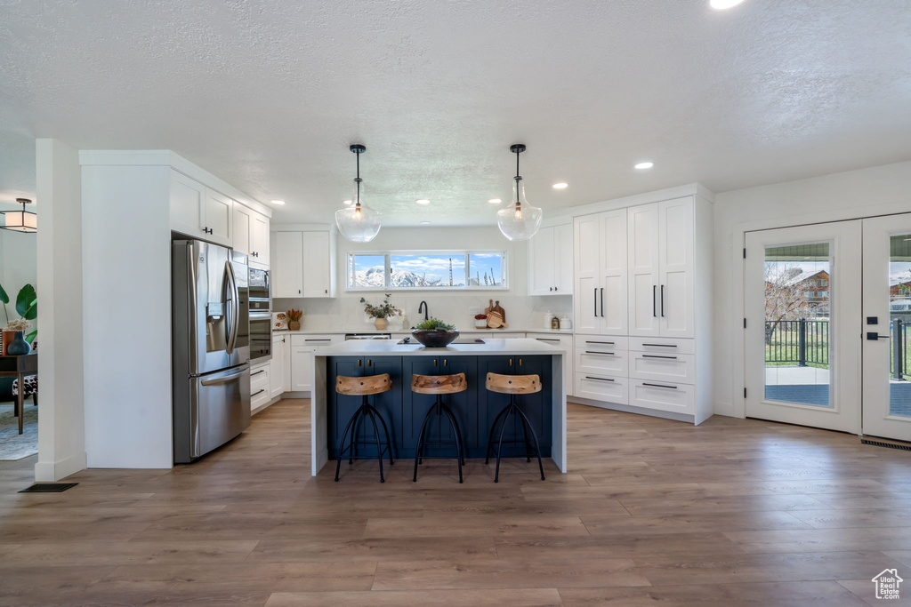 Kitchen featuring a kitchen island, white cabinets, stainless steel appliances, hardwood / wood-style flooring, and pendant lighting
