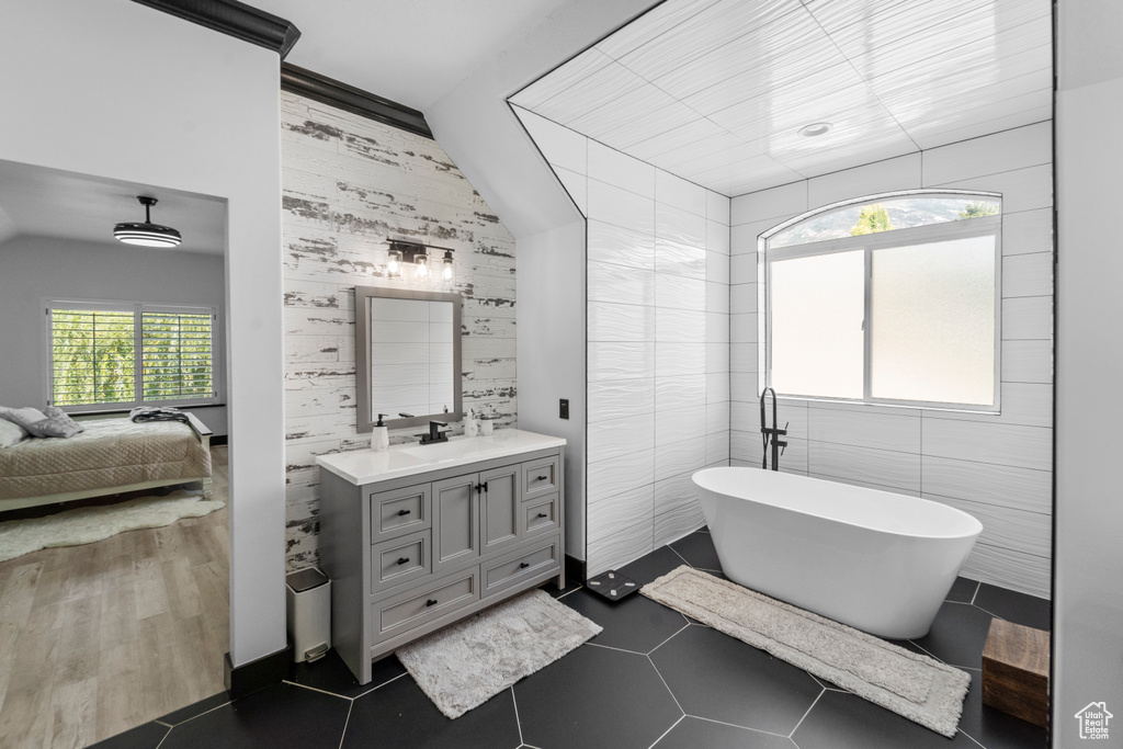 Bathroom featuring a bath to relax in, tile walls, oversized vanity, tile flooring, and vaulted ceiling