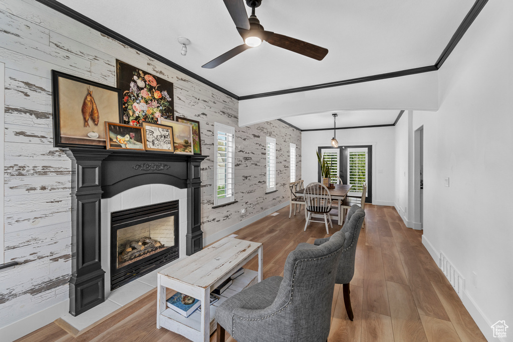 Living room featuring wood-type flooring, a fireplace, ceiling fan, and ornamental molding