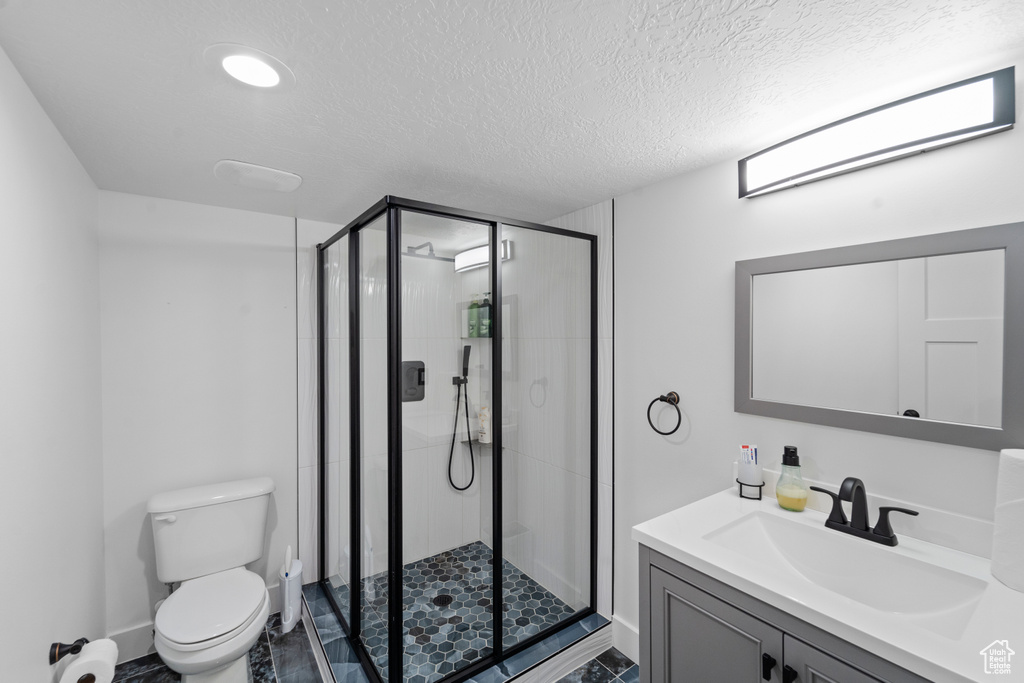 Bathroom with a shower with shower door, a textured ceiling, vanity, and toilet