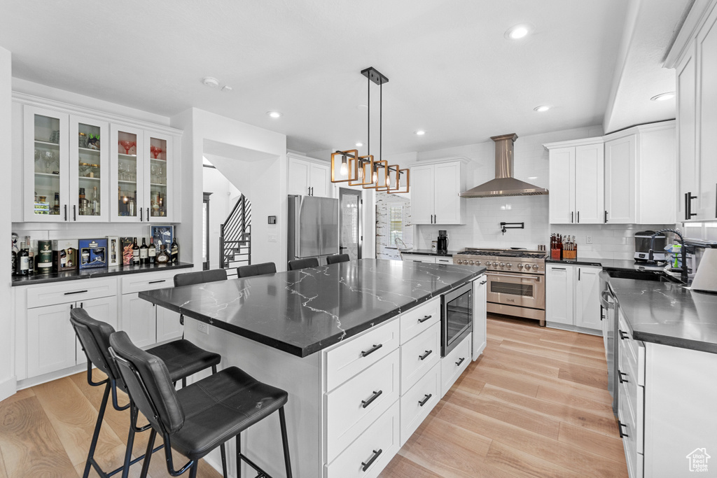 Kitchen featuring wall chimney exhaust hood, light hardwood / wood-style flooring, backsplash, appliances with stainless steel finishes, and a kitchen island