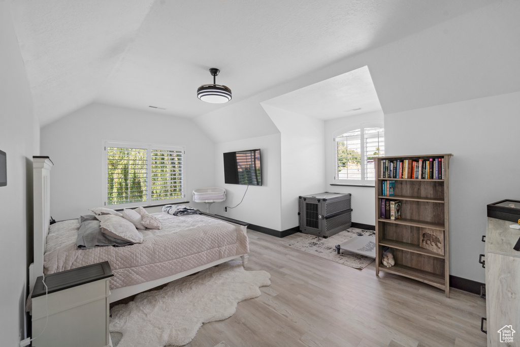 Bedroom featuring lofted ceiling, multiple windows, and light wood-type flooring