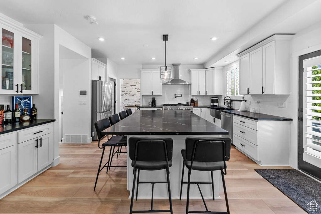 Kitchen with a center island, light hardwood / wood-style flooring, white cabinetry, backsplash, and wall chimney range hood