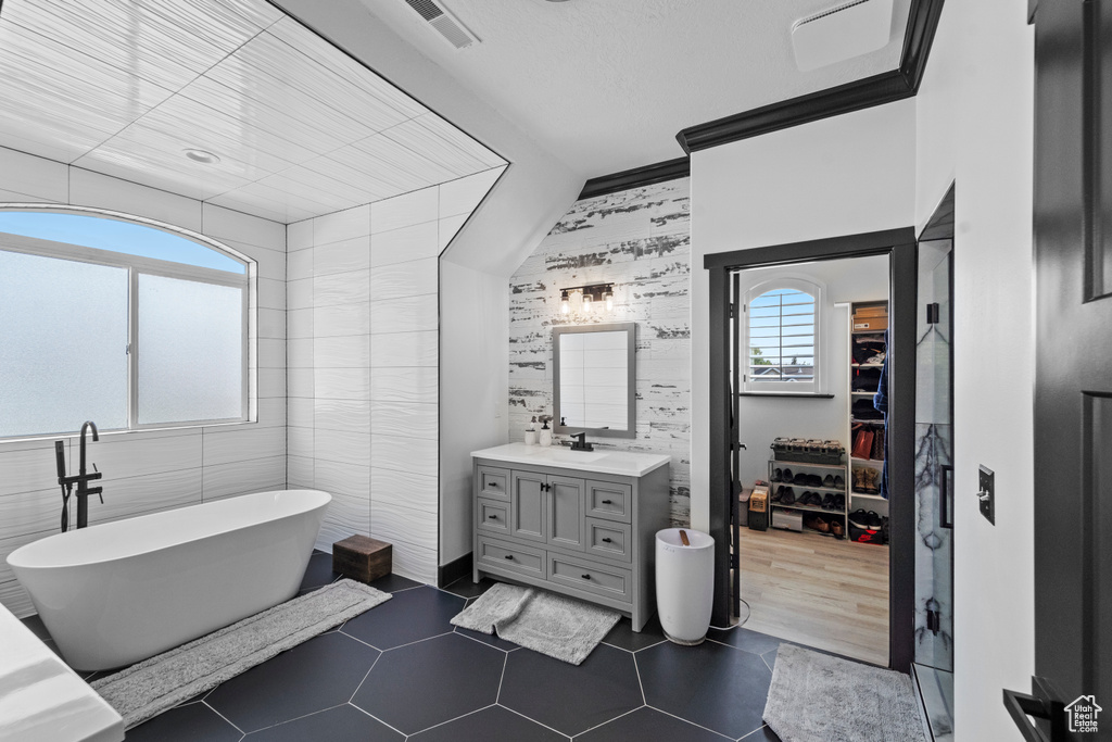Bathroom with vanity, tile flooring, tile walls, and a bath