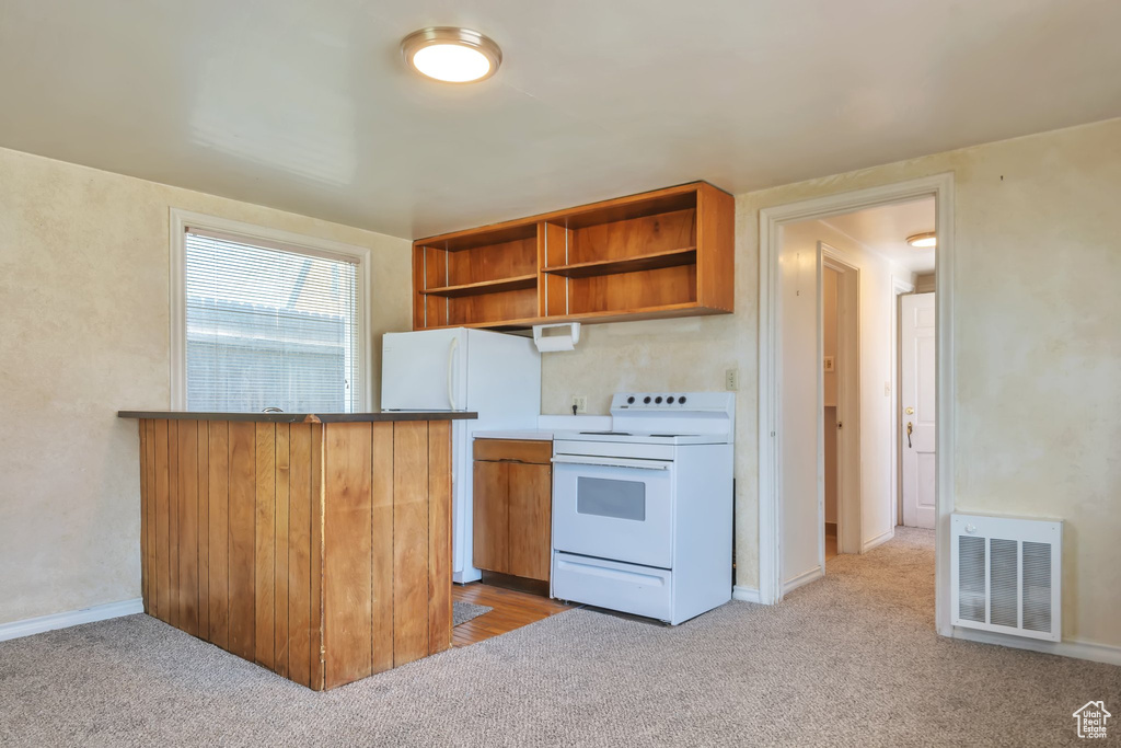 Kitchen with kitchen peninsula, light carpet, and white appliances