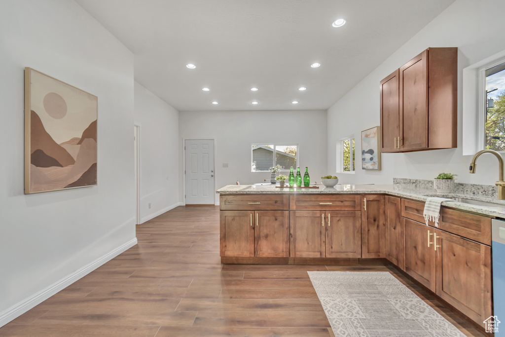Kitchen featuring sink, dishwasher, light wood-type flooring, kitchen peninsula, and light stone countertops