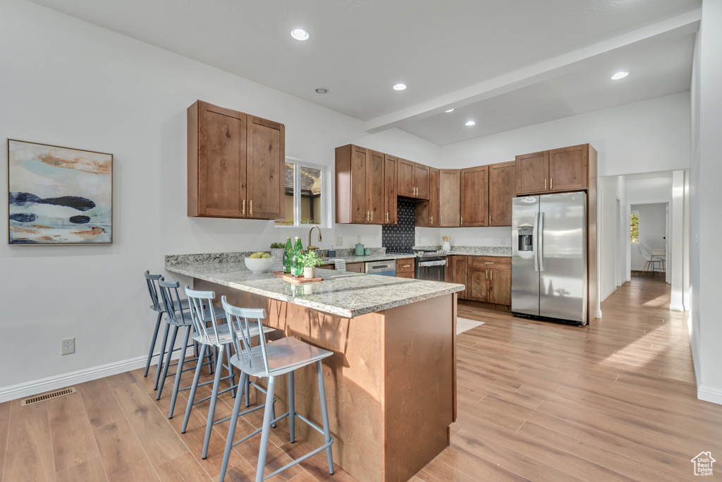 Kitchen with appliances with stainless steel finishes, a breakfast bar area, light hardwood / wood-style floors, and a healthy amount of sunlight