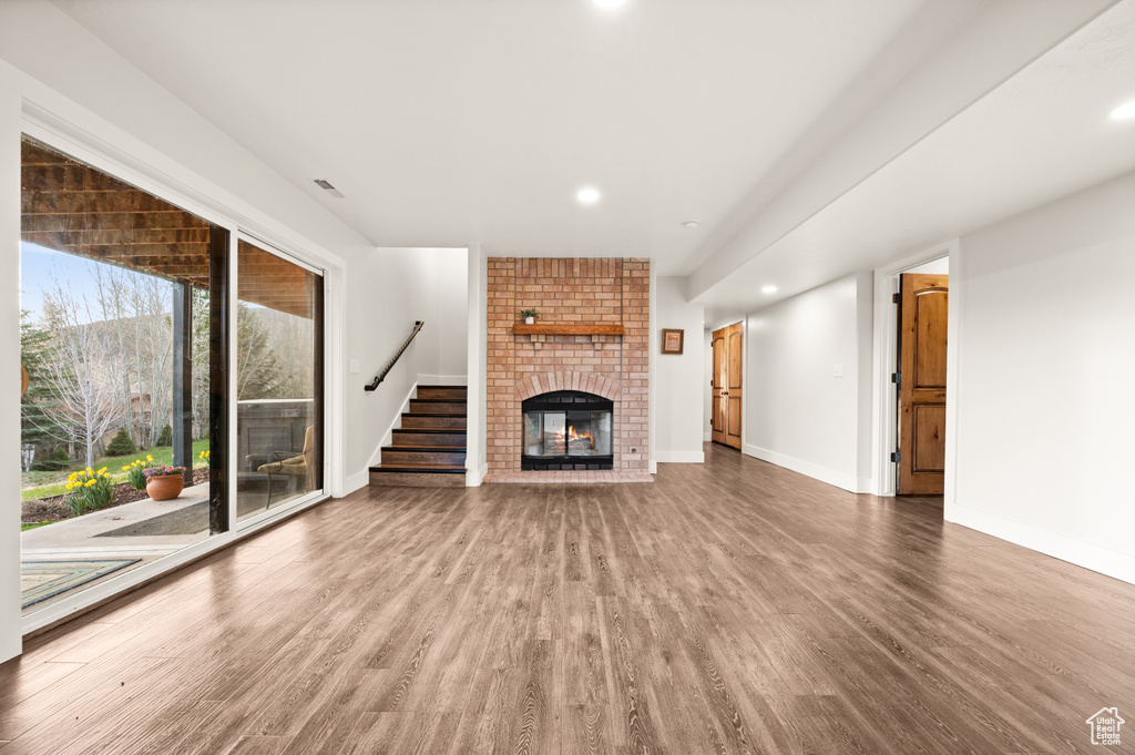 Unfurnished living room featuring a fireplace, hardwood / wood-style floors, and brick wall