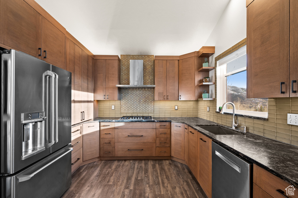 Kitchen with dark hardwood / wood-style flooring, wall chimney range hood, stainless steel appliances, sink, and tasteful backsplash