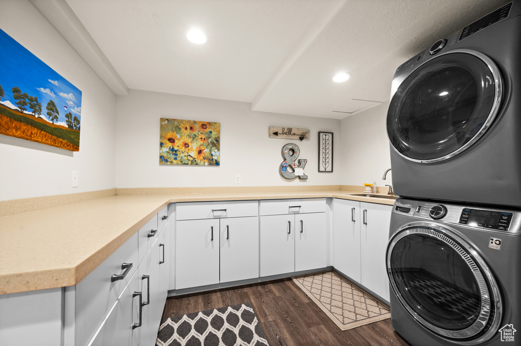 Laundry room featuring dark hardwood / wood-style flooring, cabinets, sink, and stacked washer and clothes dryer