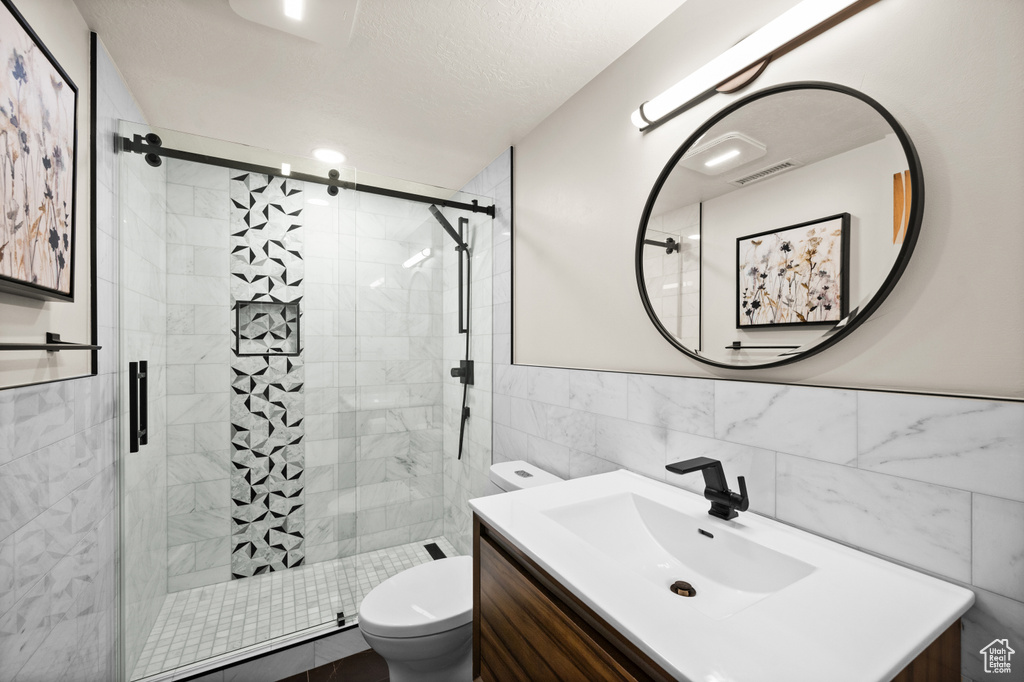 Bathroom featuring vanity, an enclosed shower, toilet, and tile walls