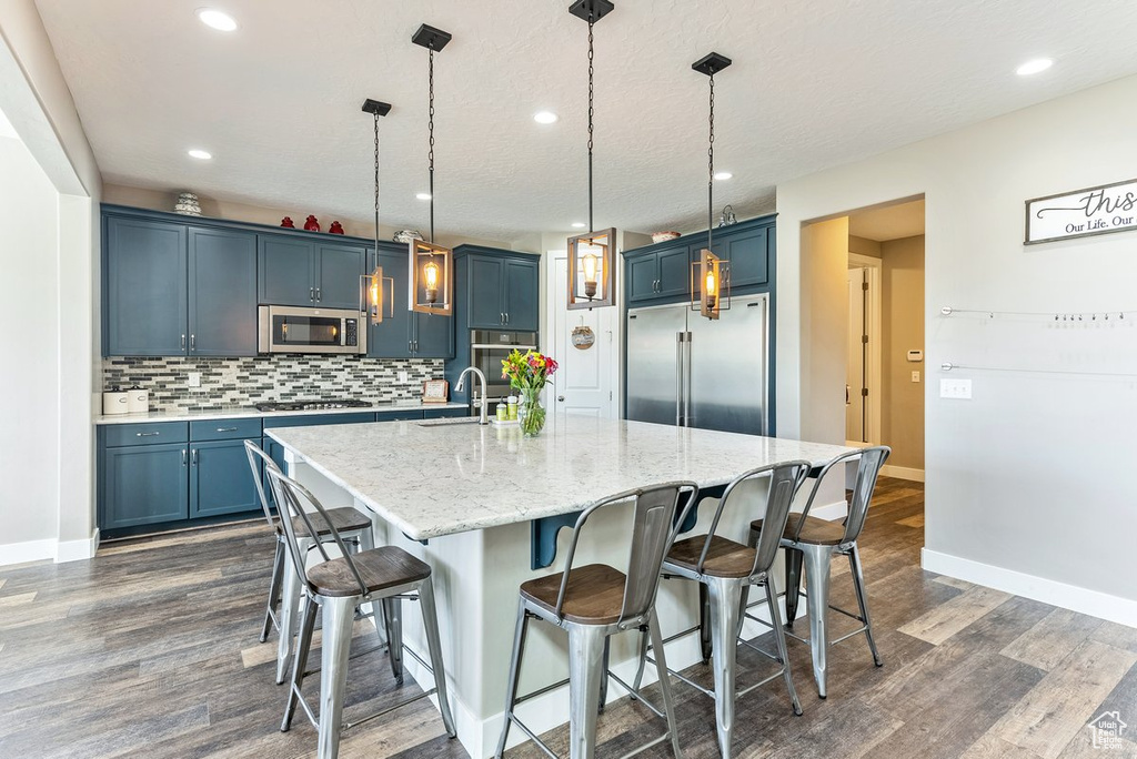 Kitchen featuring appliances with stainless steel finishes, decorative light fixtures, blue cabinetry, and a kitchen bar