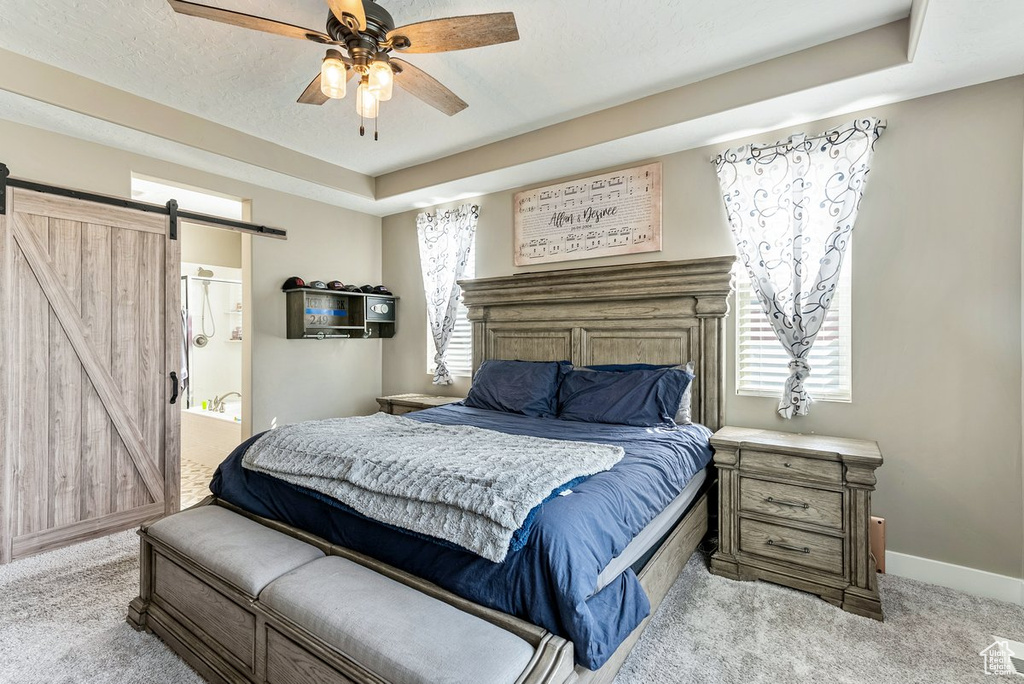 Carpeted bedroom featuring ensuite bath, a barn door, ceiling fan, and a raised ceiling