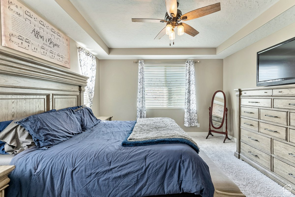 Carpeted bedroom featuring a textured ceiling, ceiling fan, and a tray ceiling