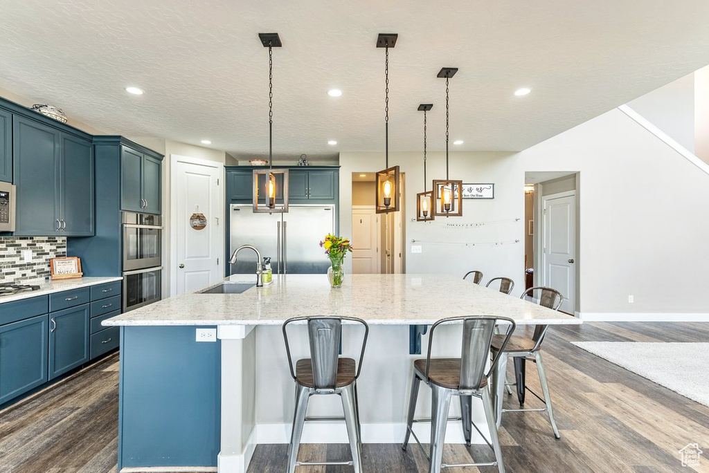 Kitchen with appliances with stainless steel finishes, hanging light fixtures, a large island, dark wood-type flooring, and sink