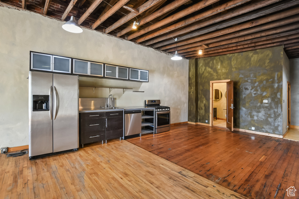 Kitchen with appliances with stainless steel finishes, a towering ceiling, stainless steel counters, beam ceiling, and hardwood / wood-style flooring