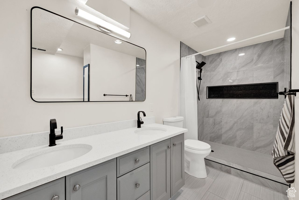 Bathroom featuring walk in shower, large vanity, toilet, tile flooring, and double sink