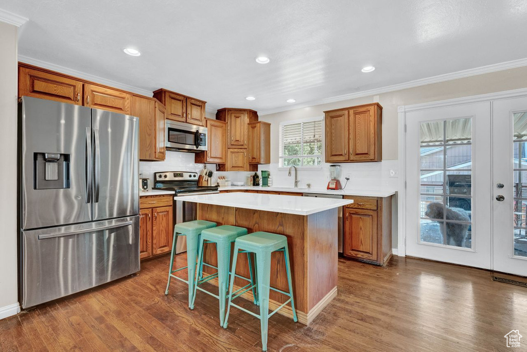Kitchen featuring a center island, ornamental molding, appliances with stainless steel finishes, and wood-type flooring