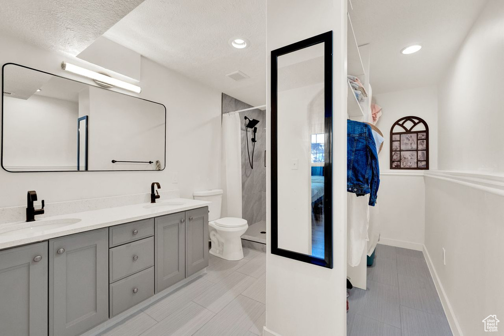 Bathroom with double vanity, a textured ceiling, toilet, and tile flooring