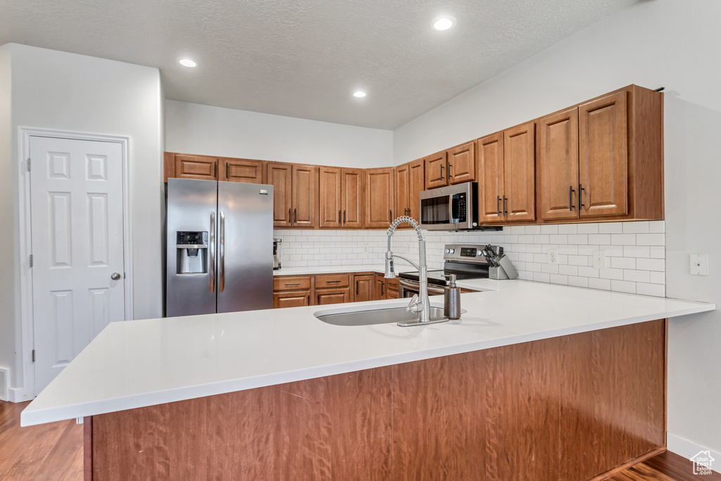 Kitchen featuring backsplash, light hardwood / wood-style flooring, stainless steel appliances, and kitchen peninsula