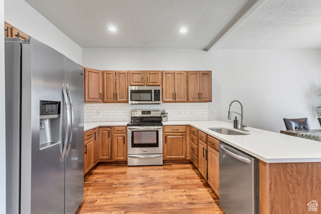Kitchen featuring kitchen peninsula, backsplash, stainless steel appliances, sink, and light wood-type flooring