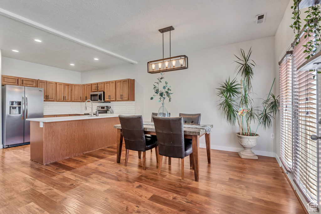 Interior space with decorative light fixtures, light wood-type flooring, kitchen peninsula, appliances with stainless steel finishes, and tasteful backsplash