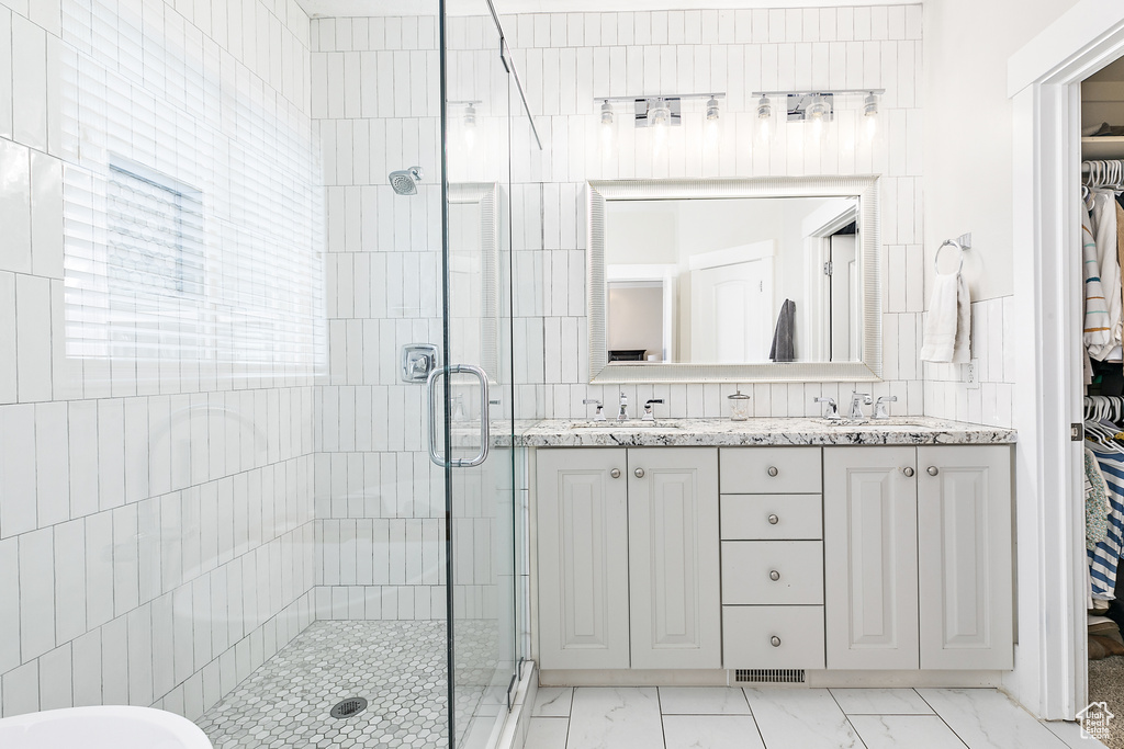 Bathroom featuring tile flooring, double sink vanity, a shower with door, and tile walls