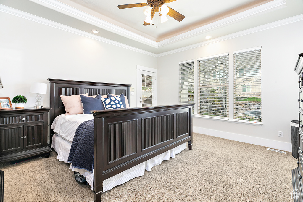 Carpeted bedroom with ceiling fan, crown molding, and a raised ceiling