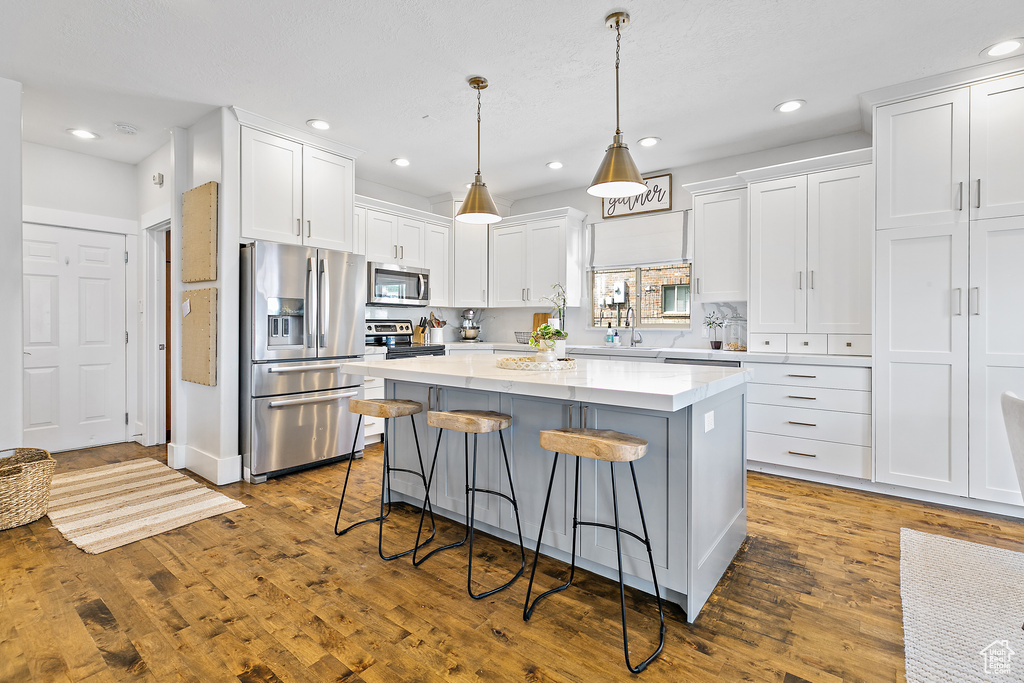 Kitchen with a kitchen island, hanging light fixtures, white cabinets, stainless steel appliances, and hardwood / wood-style flooring