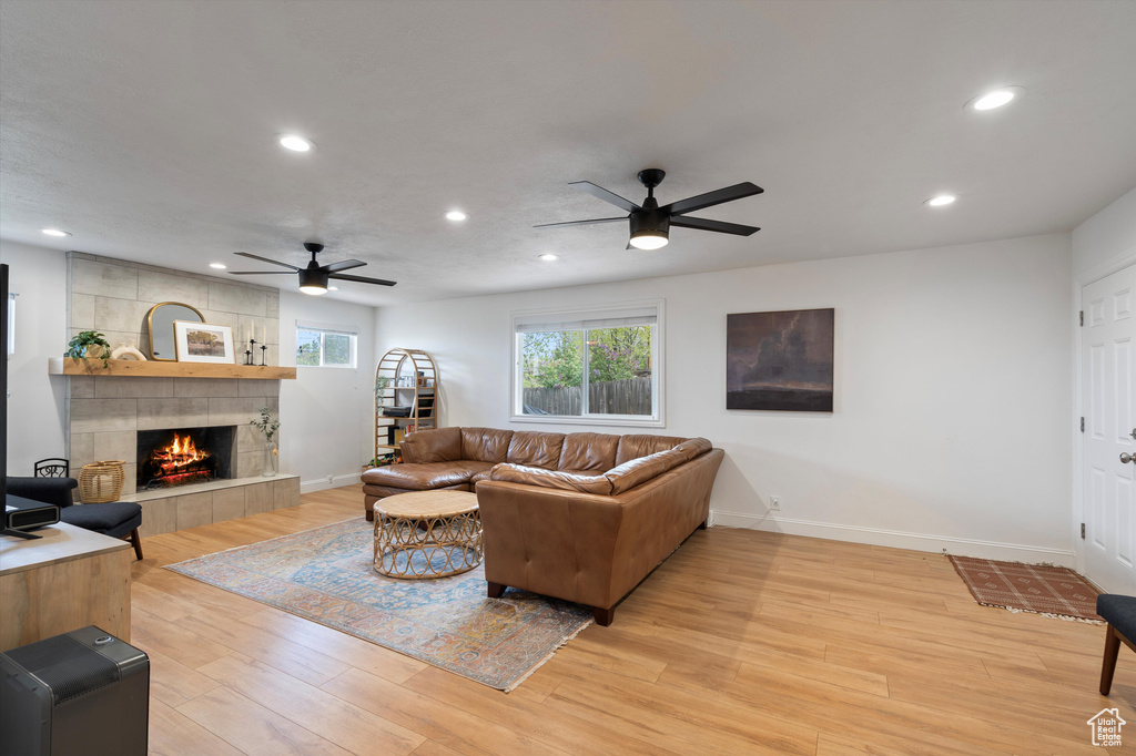 Living room with ceiling fan, a tile fireplace, and light hardwood / wood-style floors