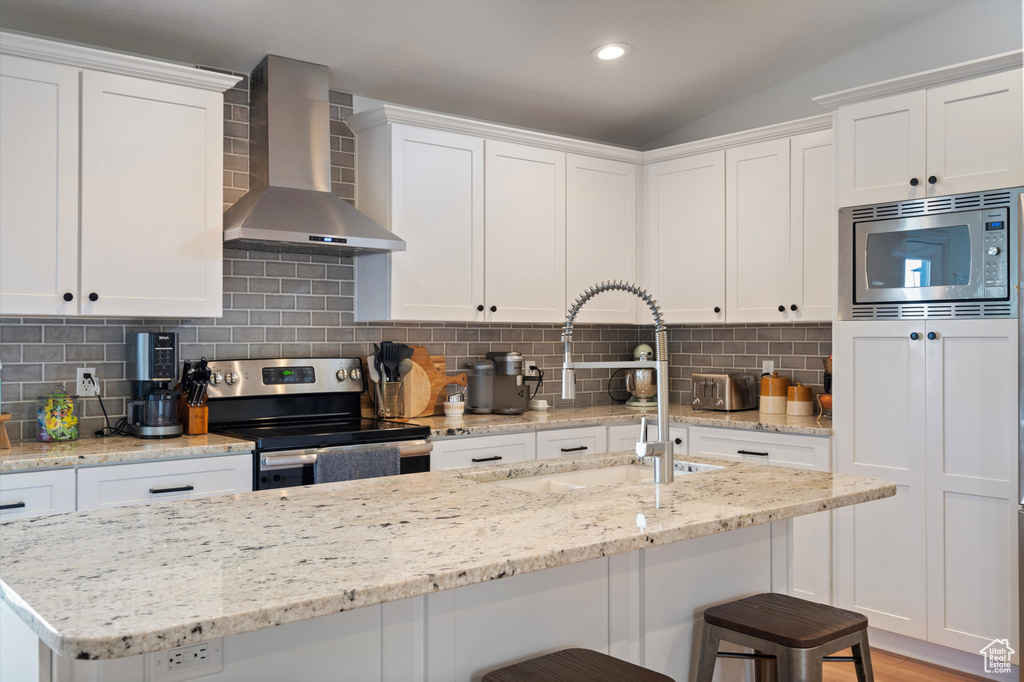 Kitchen with tasteful backsplash, appliances with stainless steel finishes, wall chimney range hood, and white cabinets