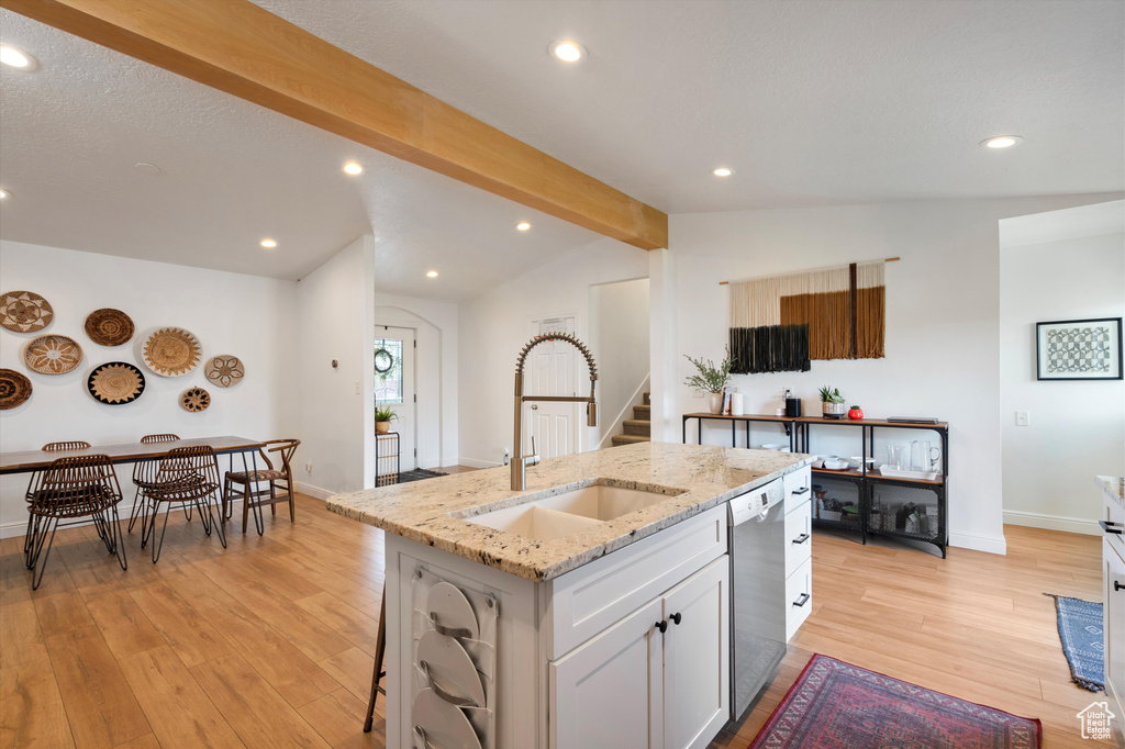 Kitchen with a center island with sink, lofted ceiling with beams, light stone counters, light wood-type flooring, and stainless steel dishwasher