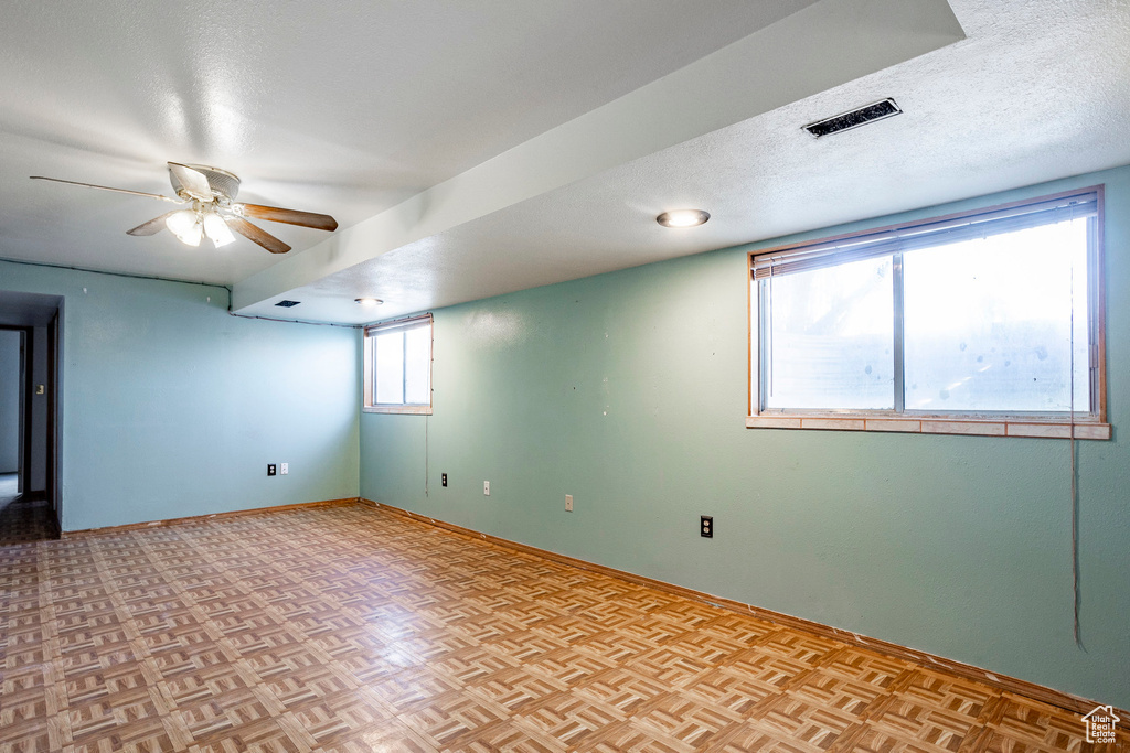 Empty room with light parquet floors, ceiling fan, and a textured ceiling