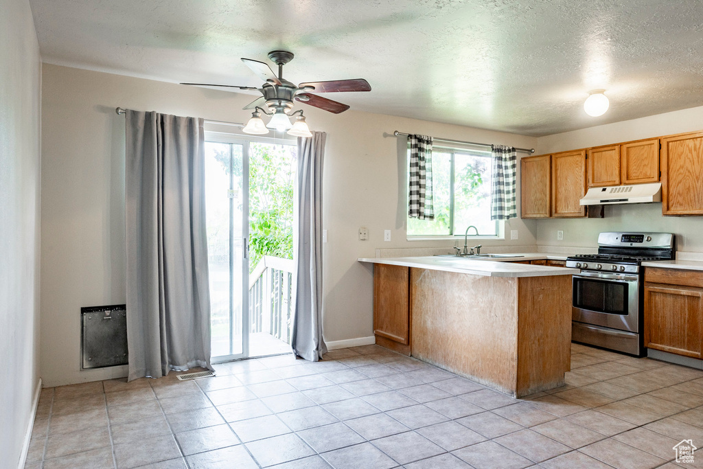 Kitchen with a healthy amount of sunlight, sink, light tile floors, and stainless steel gas range oven
