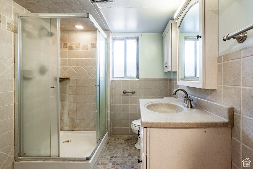 Bathroom with tile walls, large vanity, walk in shower, toilet, and tile floors